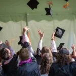 Group of graduates celebrating by tossing caps into the air during a graduation ceremony.